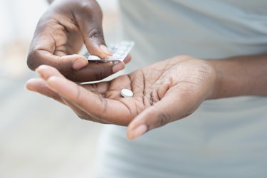 Close up of person's hand holding a pill packet and a pill for a yeast infection