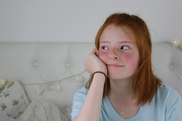 Image of red haired teenage girl with pale skin, freckles and flushed cheeks sitting in her bedroom