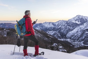 Hiker with snowshoes on mountain using smartphone apps