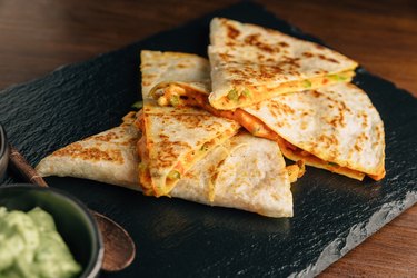 Close up Baked Chicken and Cheese Quesadillas served with Salsa and Guacamole on stone plate.
