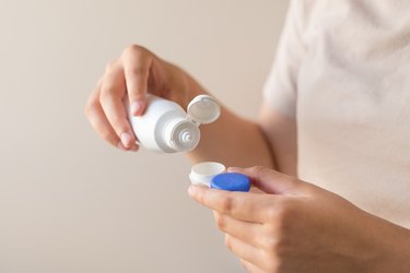 close view of a person's hands putting contact solution into a contact lens case