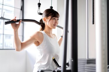 Asian woman doing a behin-the-neck lat pulldown at the gym