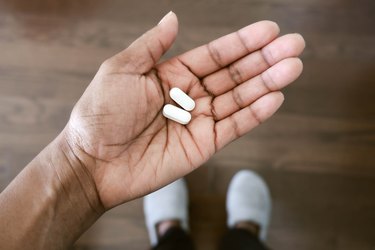 close view of a person's hand holding two pain reliever pills, as a home remedy for bunions