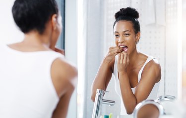 woman looking in the bathroom mirror and flossing her teeth to prevent morning breath