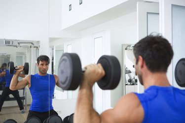 Man doing a dumbbell shoulder press in front of a mirror