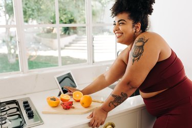 plus-size woman in workout gear leaning over kitchen countertop