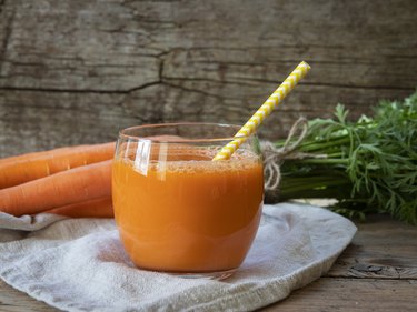 Fresh squeezed carrot juice in a glass on a wooden surface, as an example of the best drinks for heartburn