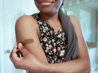 A woman taking a bandage off her upper arm after getting the COVID vaccine