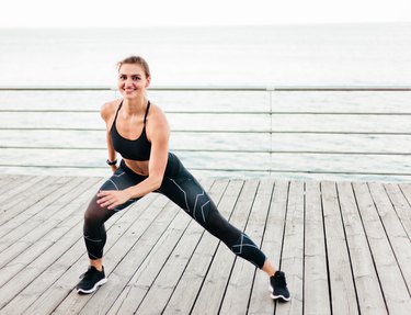 Young fit person in a black sports bra and leggings does the lateral lunge on a beach terrace