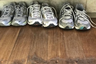 A group of very worn out tennis shoes over a wooden floor.