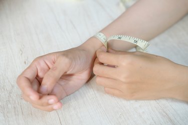 person measuring wrist with tape measure on wooden table to determine body frame size