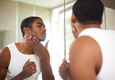 a man looking in the bathroom mirror and rubbing in retinol cream, as a natural remedy for acne