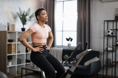 Athlete in living room using stationary bike and taking a breath.