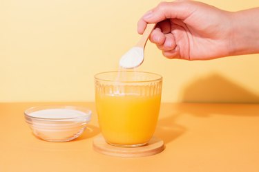 Woman adding powder from slim water packets to cup of orange Emergen-C drink for kids 14 and up