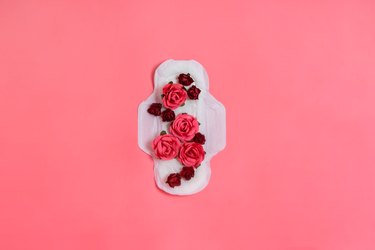 White sanitary pad with red and pink flowers on it, on a pink background, to represent period smells