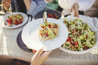 Close-up of woman serving pasta to friend at picnic table