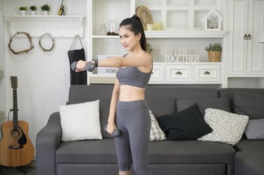 Beautiful young woman in sportswear exercising with dumpbells at home