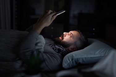 man in bed at home at night, using smartphone in dark mode for better sleep