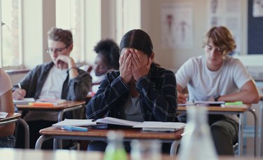 Crying female student struggling with schoolwork in a classroom.