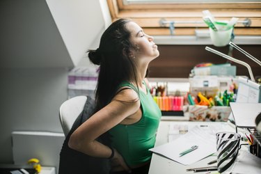 Young woman having back pain while sitting at desk