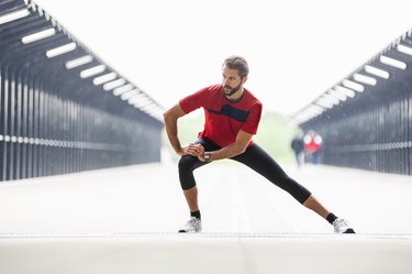 Man in a red shirt doing a side lunge leg exercise on a bridge