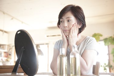 Asian woman looking at her face in a small mirror and touching her cheeks with her hands