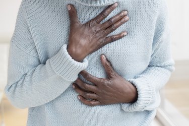 close view of a person wearing a light blue sweater with their hand on their chest because their chest feels full after eating
