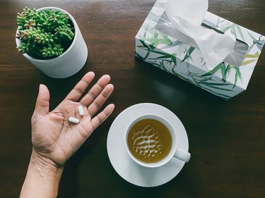 person holds pills in hand next to mug of green tea