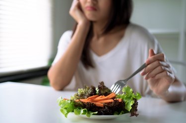 Unhappy woman picking at a plate of vegetables with a fork