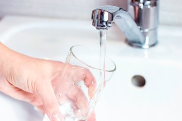 close-up photo of a hand holding a glass under a running faucet in a white sink where the tap water has a balanced pH value