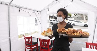 戴着口罩的女服务员在户外帐篷里为顾客提供食物