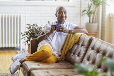 Senior woman sitting on a brown couch enjoying a cup of coffee and it's longevity benefits