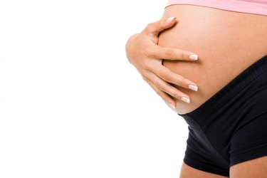 Close-up of pregnant person holding their stomach, while wearing bike shorts, against a white background.