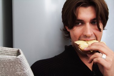 Young man reading newspaper eating bread and cheese