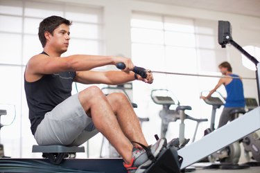 Young man exercising on rowing machine in gymnasium