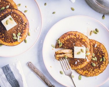 Pumpkin protein pancakes with an orange hue topped with pumpkin seeds and butter