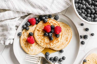 Cottage cheese pancakes on a plate, topped with fresh berries and syrup