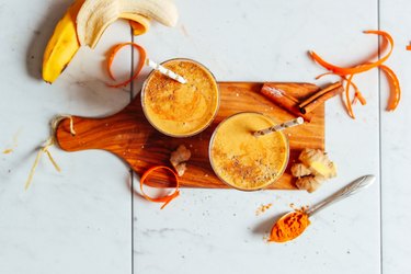 Creamy Golden Milk Smoothie in two glasses on wooden cutting board sitting on marble countertop.