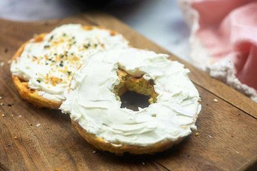 Low-Carb Bagel with cream cheese and seasonings on a wooden cutting board.