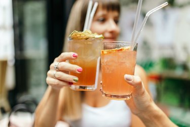 two young adults toast with glasses of a light orange cortisol cocktail outside