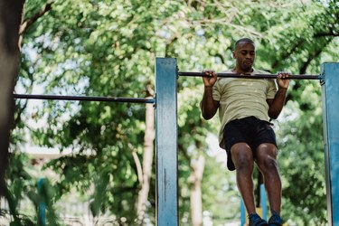 Man doing kipping pull-up in park.