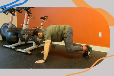 a man in a green T-shirt and pants and black sneakers demonstrates a leopard crawl exercise performing a HIIT resistance band workout in a gym