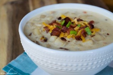 A white bowl of Loaded Baked Potato Soup on a blue tablecloth