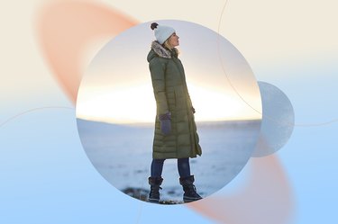 a young adult wearing an olive green Eddie Bauer Lodge Down Duffle Coat and a white beanie outside with snow in the background