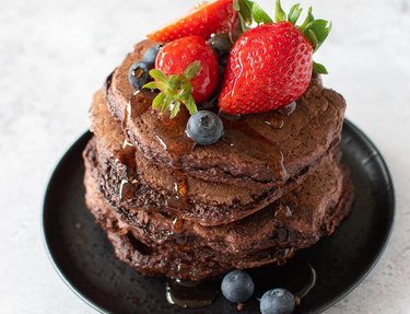 A stack of chocolate protein pancakes topped with berries and syrup