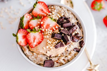 Breakfast recipe for skin including oatmeal with strawberries and dark chocolate pieces on top in a white bowl on countertop.