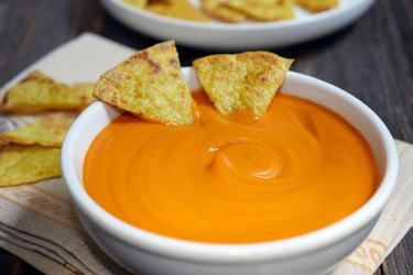 Sweet potato nacho cheese dip in a while bowl with tortilla chips.