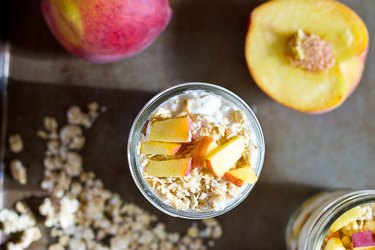 An aerial shot of glass jar with granola and sliced peaches on top