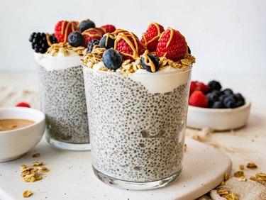 Two servings of protein chia pudding in clear glasses, topped with berries, granola and nut butter