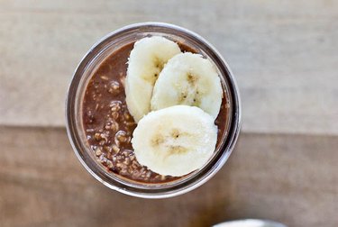 An aerial shot of chocolate oats in a glass jar, topped with banana slices.